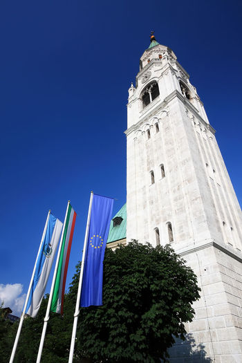 Low angle view of flags by clock tower against clear blue sky
