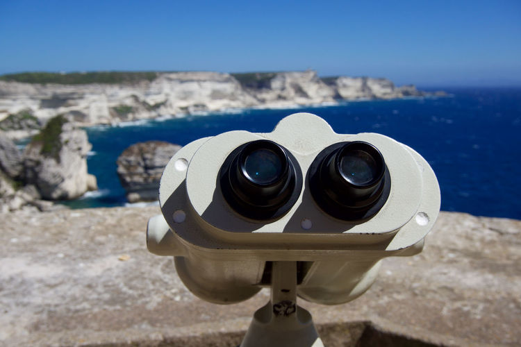 Close-up of coin-operated binoculars against sea and rocky shore