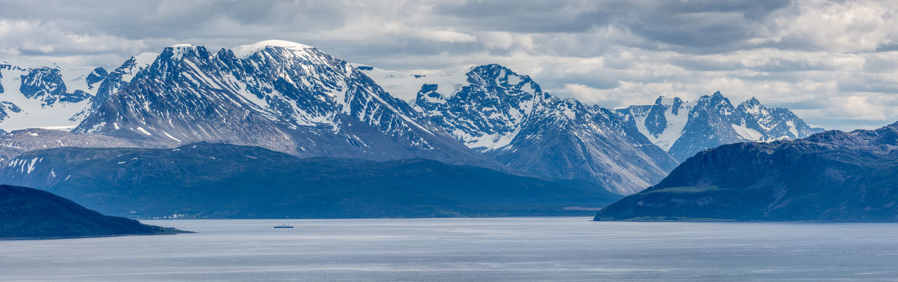 Panoramic shot of sea and snow covered mountains against cloudy sky