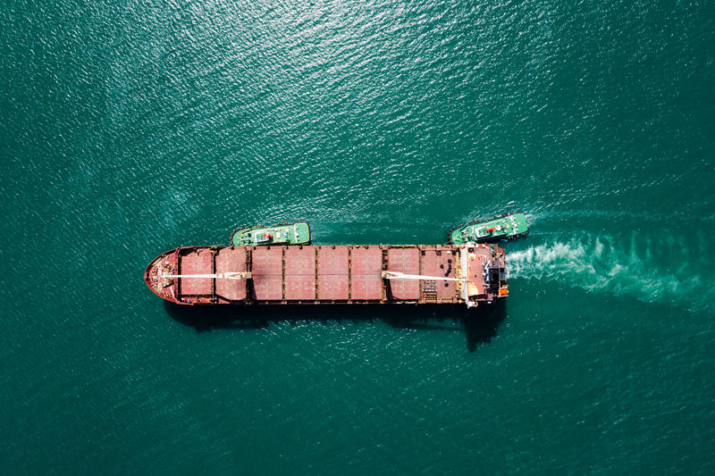 Red oil ship tank and tugboat sailing on green sea photograph aerial from drone point of view