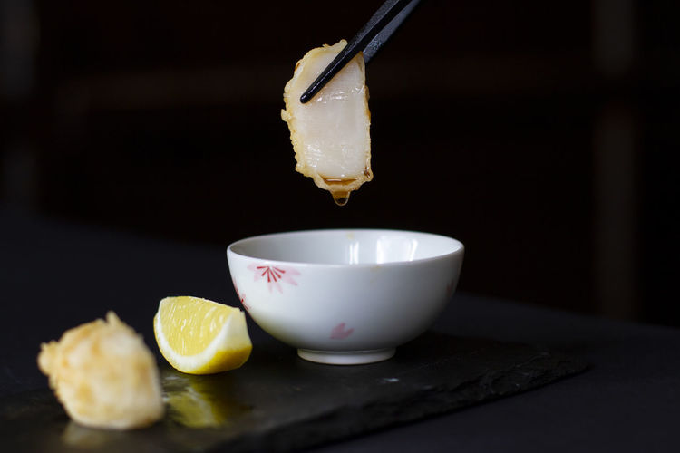 Tempura scallop dipped in soya sauce with chopsticks and lemon on the side 
