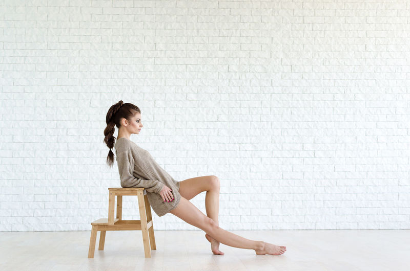 Side view of woman sitting on chair against wall
