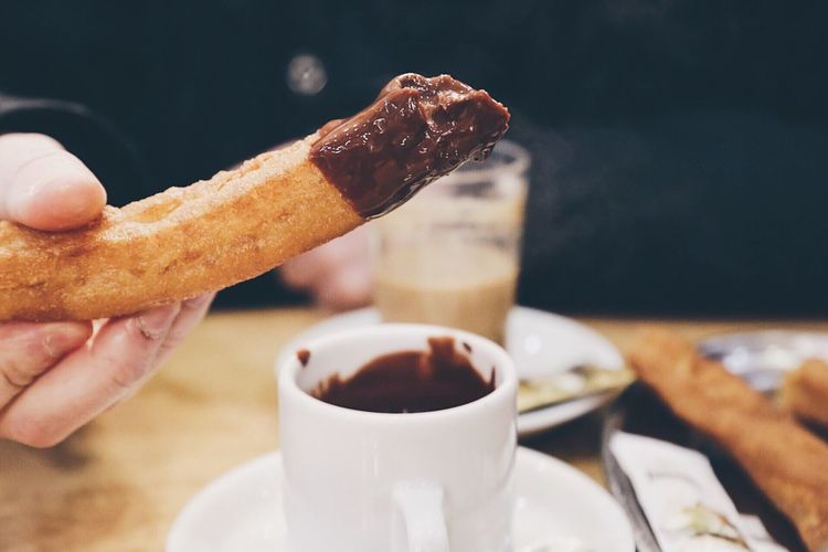 Cropped image of person dipping churro in chocolate at table