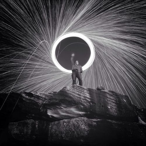 Low angle view of man spinning steel wool on rock at night