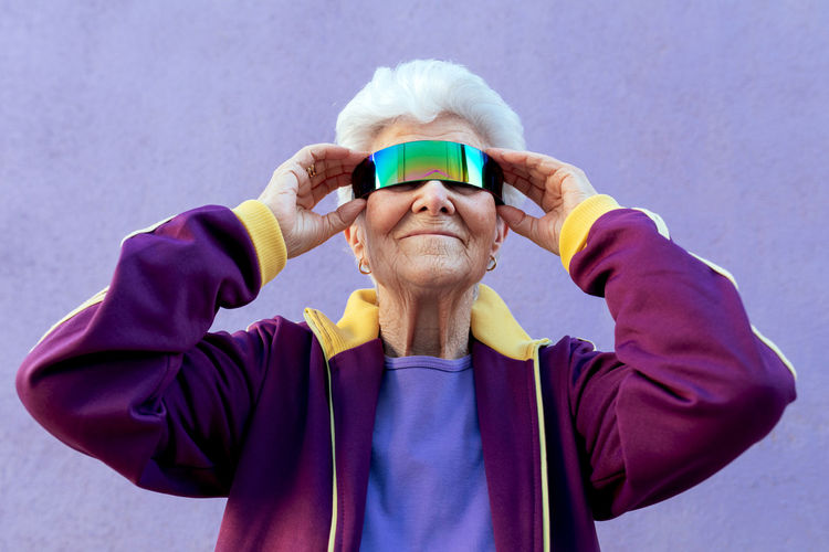 Cheerful elderly female athlete with gray hair in sportswear and blindfold on violet background