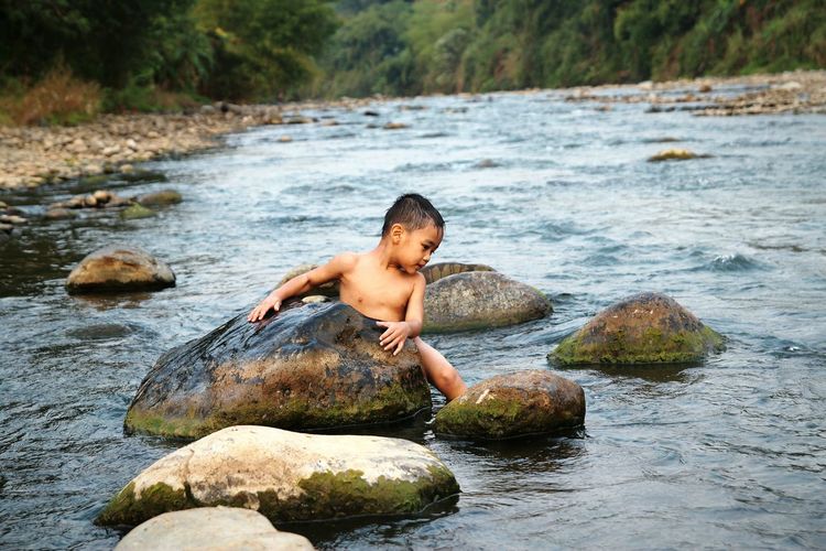 Shirtless boy holding rock in river