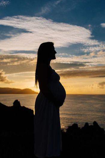 Silhouette pregnant woman standing on field by sea against sky