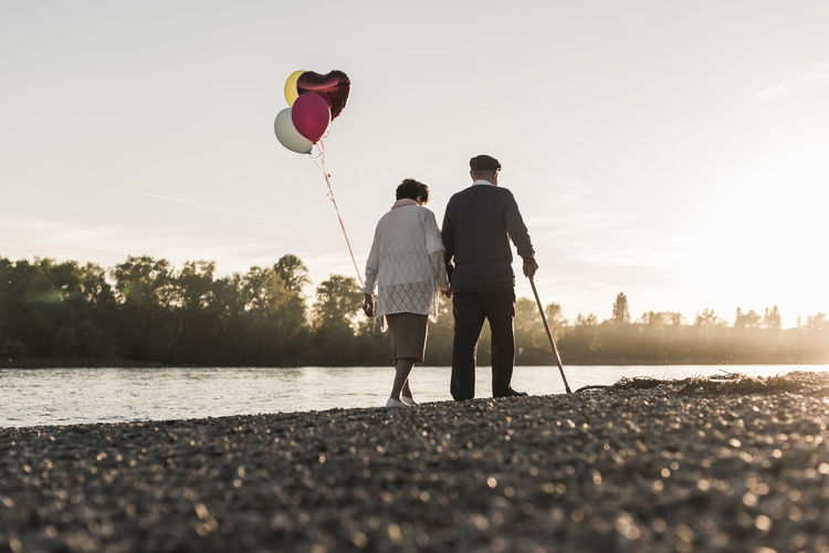 Back view of senior couple with balloons strolling at riverside in the evening
