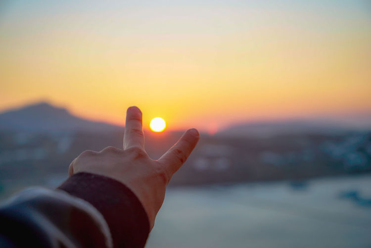 Close-up of hand gesturing peace sign against sky during sunset