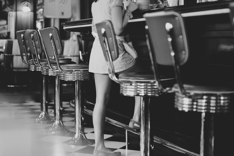 Low section of woman standing amidst chairs at restaurant