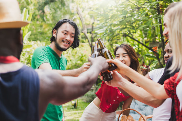 Cheerful friends toasting beers while standing outdoors