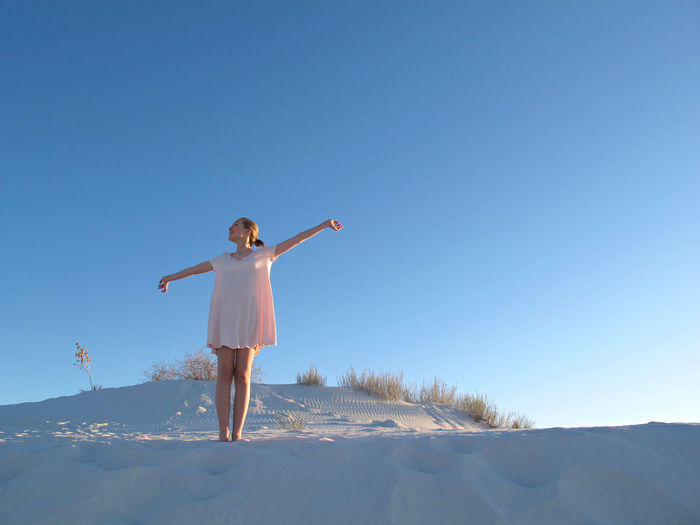 Girl standing on sand against clear blue sky