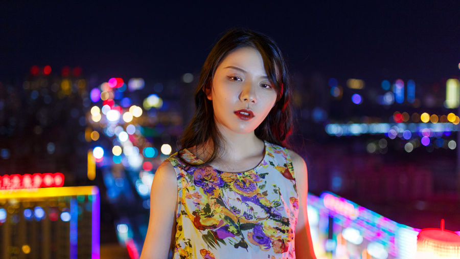 Portrait of woman standing against illuminated city at night