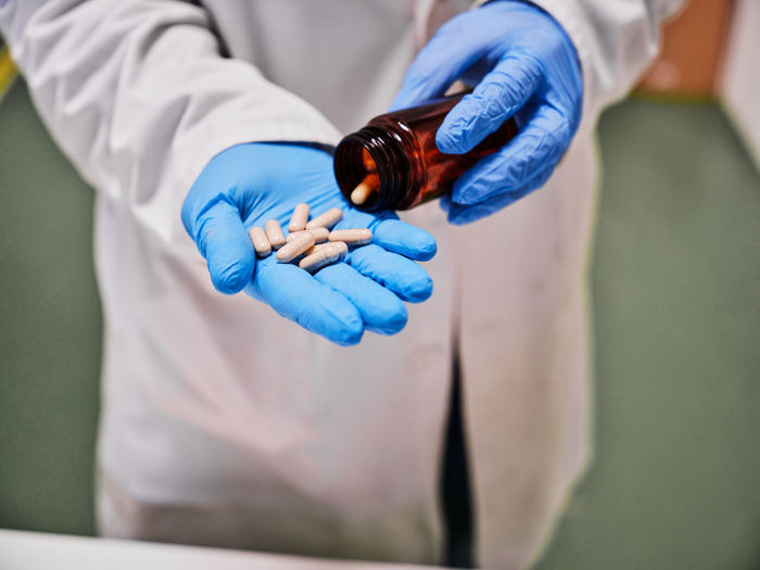 Crop anonymous scientist in protective gloves standing with pile of capsules in laboratory