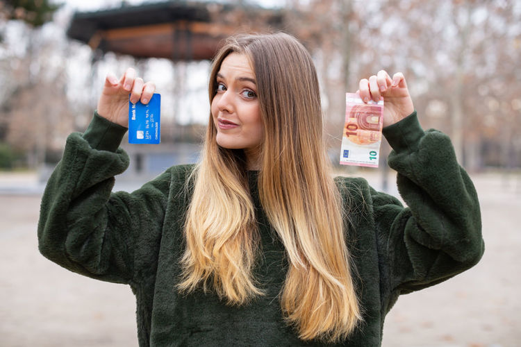 Portrait of woman holding credit card and money while standing outdoors