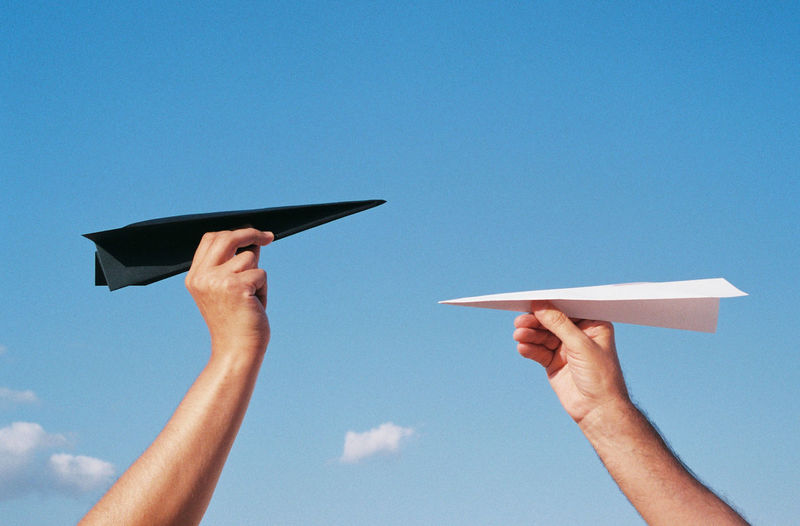 Low angle view of person hand with paper plane against blue sky