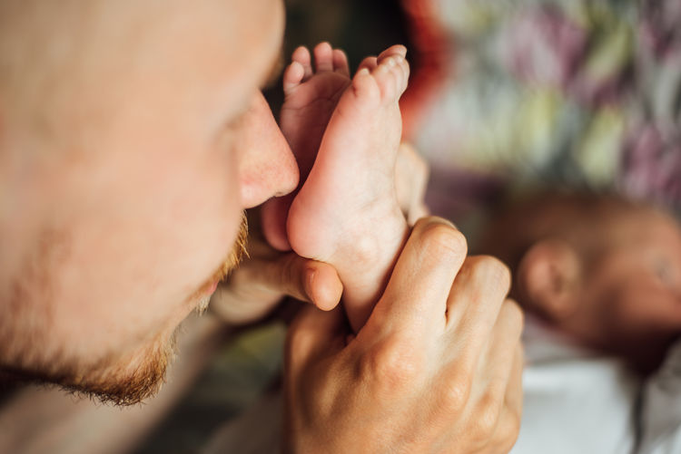 Close-up of father holding newborn son feet on bed