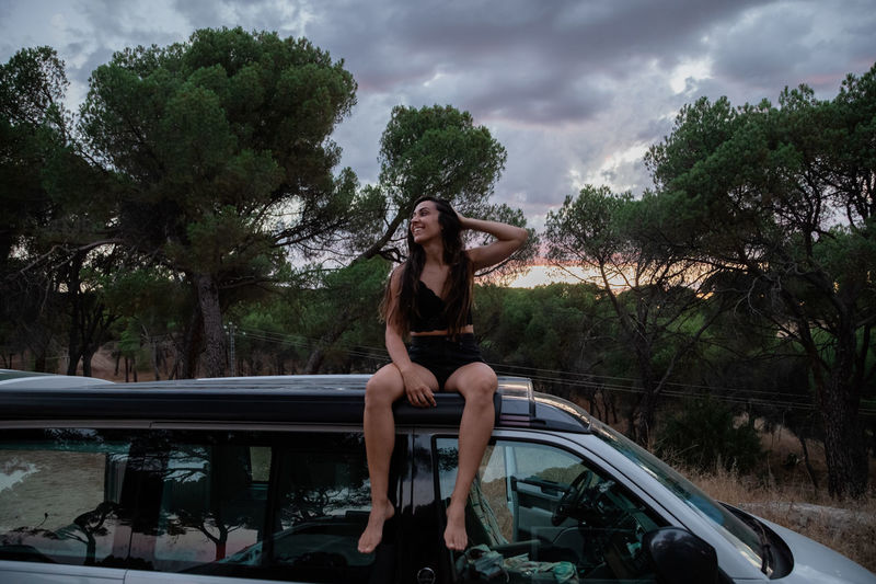 Woman sitting on car against trees