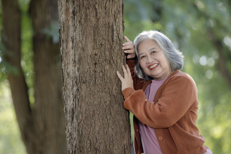 Portrait of young woman standing by tree trunk