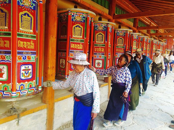 Smiling people walking by prayer wheels at temple 
