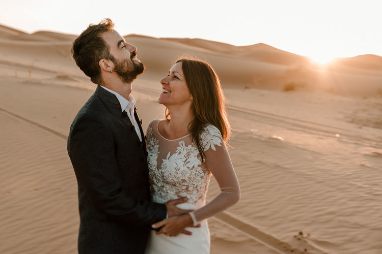 A couple in their wedding dresses in the desert are having fun while posing in the desert.