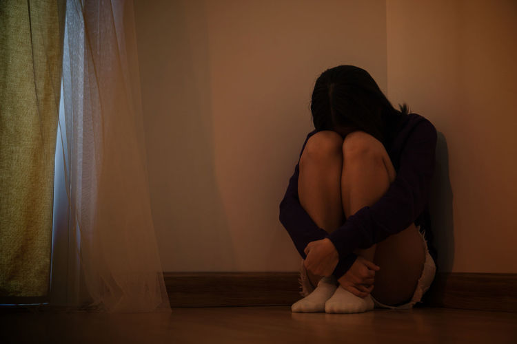 Sad young woman hugging knees at home