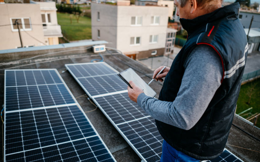 Man examining solar panel through digital tablet on roof
