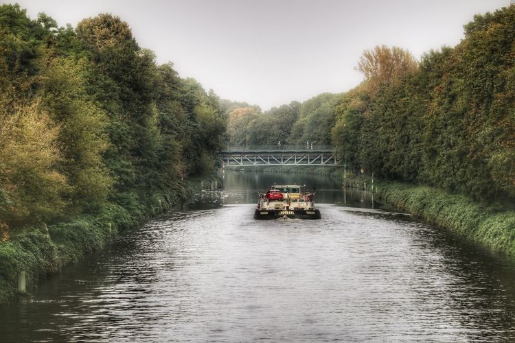 Boat sailing on river by trees against sky