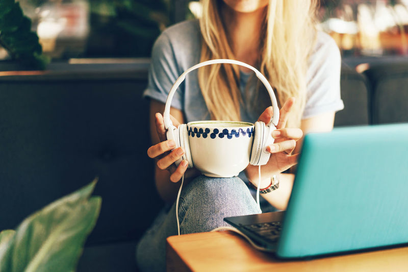 Close-up female hands are holding a big mug with headphones