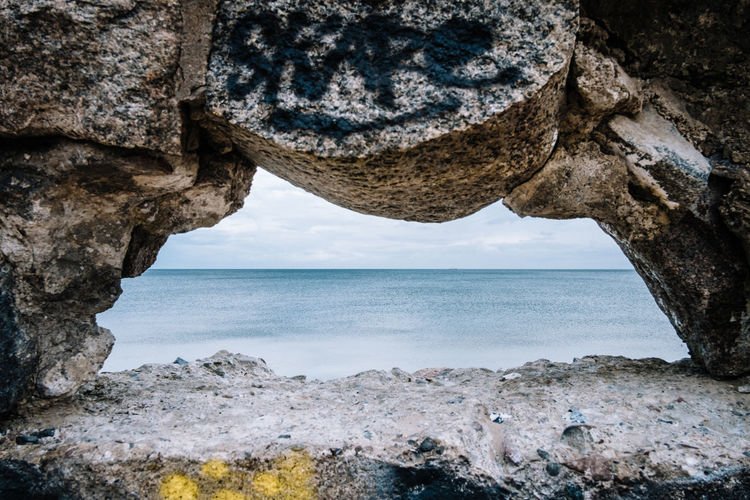 Hole in wall by sea against sky