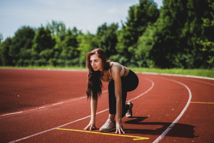 Full length of young woman at starting line on sports track