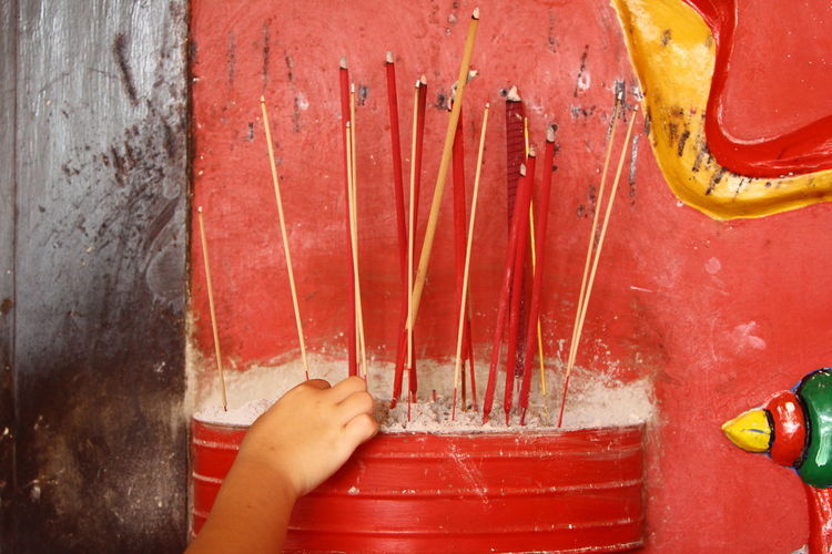 Close-up of hand holding incense in red barrel