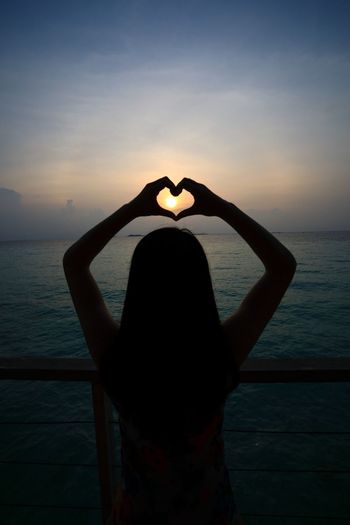 Silhouette of woman with heart shape against sea during sunset