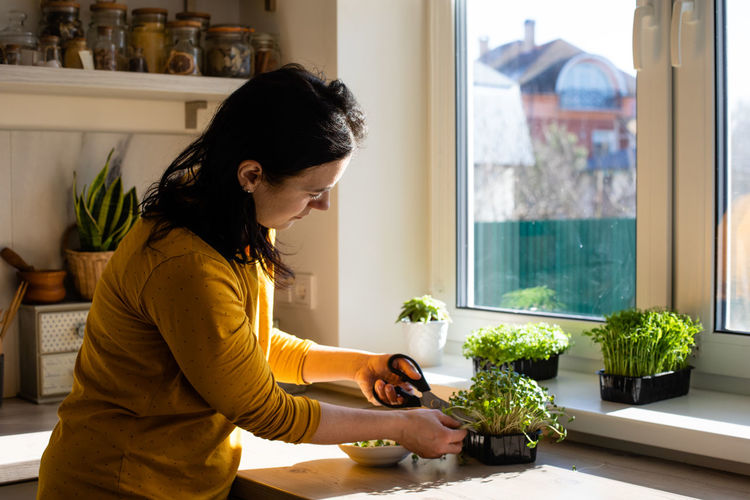 Side view of woman looking at potted plant at home