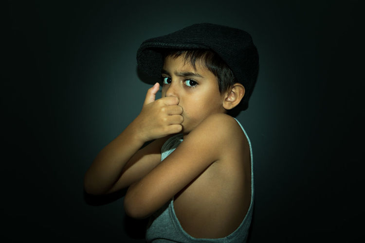 Portrait of boy with hands covering mouth against black background