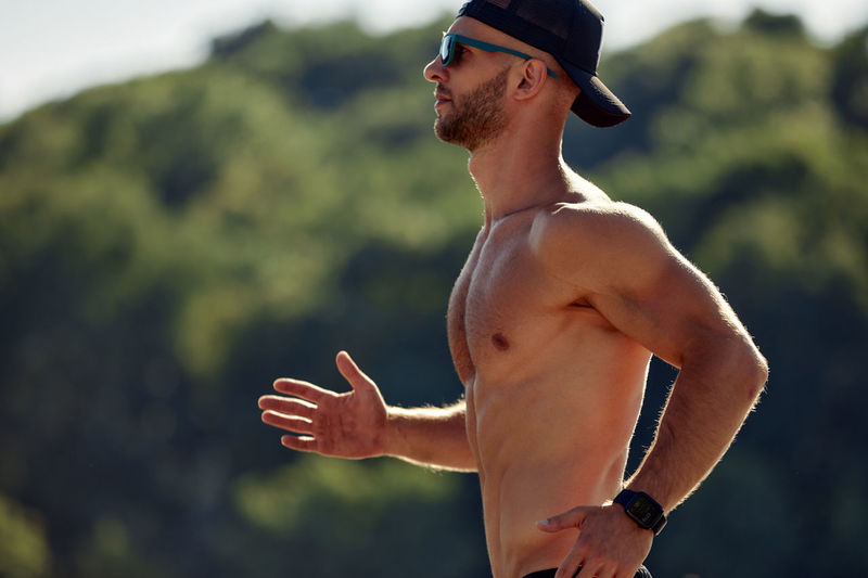 Rear view of shirtless man with arms raised standing outdoors