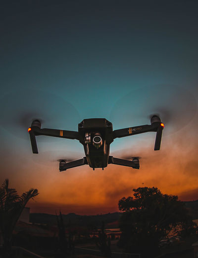 Low angle view of drone flying against sky at sunset
