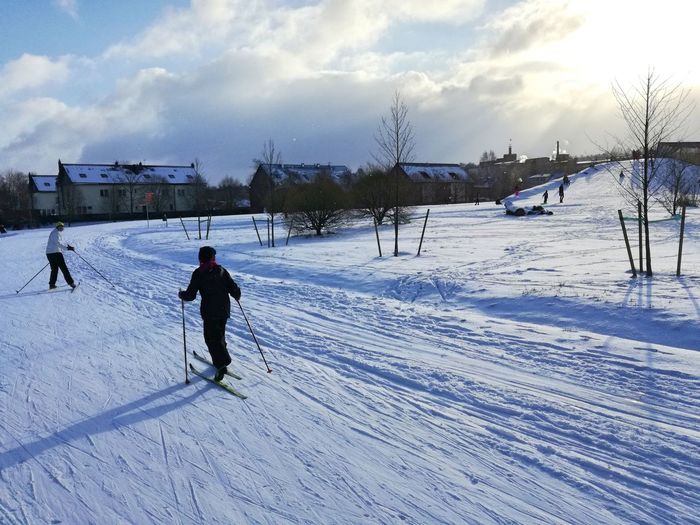 People skiing on snow covered field against sky