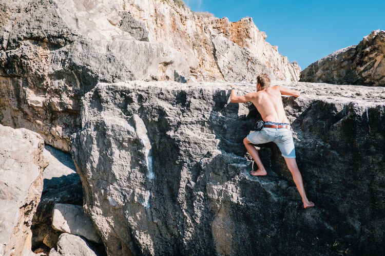 Full length of shirtless man standing on cliff against sky