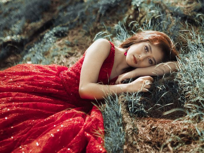 Portrait of woman in red dress lying on field