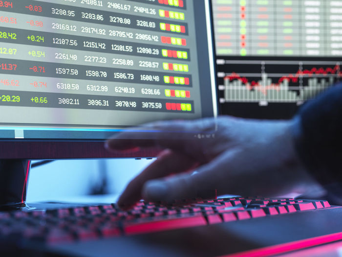 Hands of trader typing on keyboard in front of computer monitor displaying stock market data