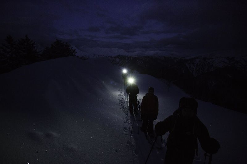 Silhouette people on snowcapped mountain against sky at night