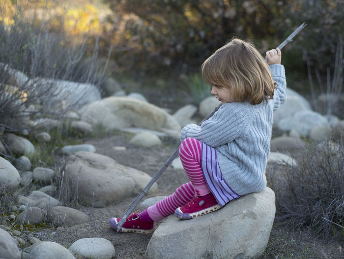 Side view of girl sitting on rock