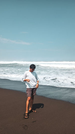 Full length of young man on beach against sky