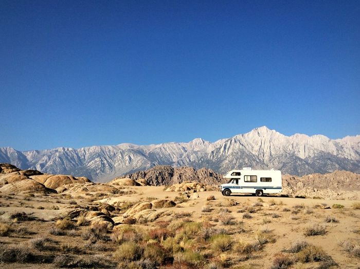 Travel trailer on field by rocky mountains against clear blue sky