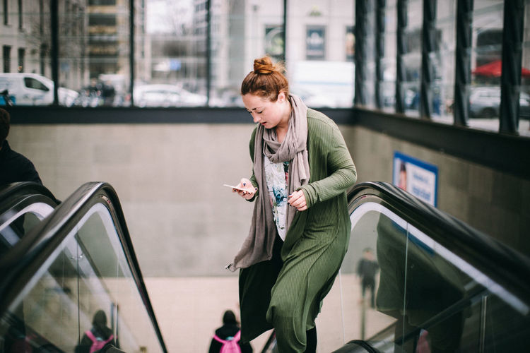Full length of young woman using mobile phone in bus