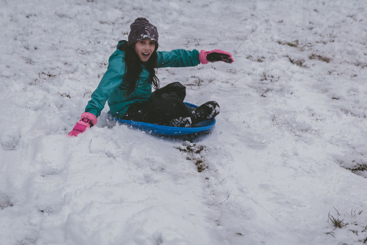 Full length of girl sitting on bobsled in snow