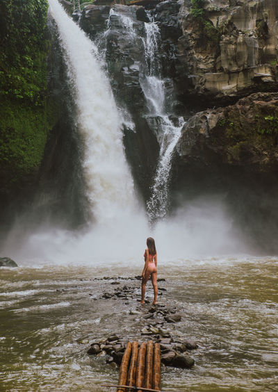 Young woman standing against waterfall
