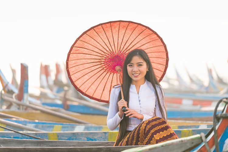 Portrait of smiling young woman holding umbrella standing outdoors