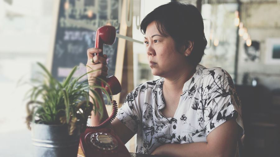 Serious woman holding telephone receiver by table